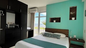 Une chambre à coucher avec un lit, une armoire, une table de chevet, une plante en pot et une vue sur l’extérieur.