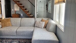Una sala de estar con un sofá seccional gris, una escalera de madera y un ventilador de techo.