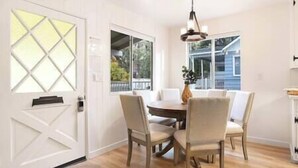 A dining room with a round table and four chairs, a window with a view of the outside, and a door with a geometric design. - NEW! Hello Big Bear: Billiards, Airhockey, Firepit (Big Bear Lake)