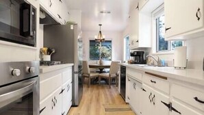 A modern kitchen with white cabinetry, stainless steel appliances, and a wooden floor. - NEW! Hello Big Bear: Billiards, Airhockey, Firepit (Big Bear Lake)