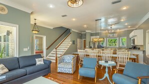 A spacious living room with a sofa, chairs, a coffee table, and a staircase leading to a dining area with a kitchen in the background.