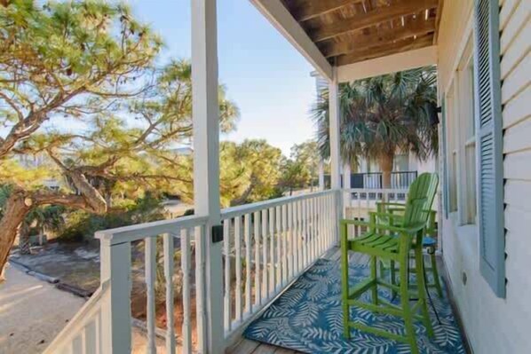 A covered porch with a white railing, two green chairs, and a patterned mat. - Pet Friendly- St George Island Sleeps 16- Pool Margarita Machine (Saint George Island)