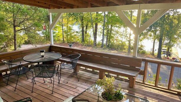 Una terraza de madera con una mesa de vidrio, sillas de metal y un banco.