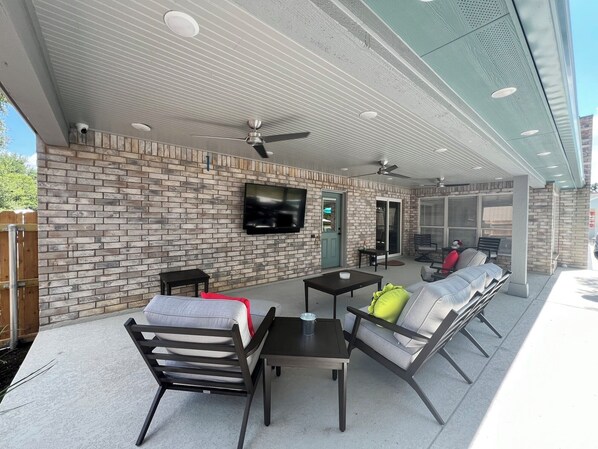 Une terrasse extérieure avec des murs en briques, un téléviseur à écran plat, des ventilateurs de plafond et du mobilier d’extérieur.