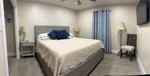Une chambre à coucher avec un lit, une table de chevet, une lampe, une chaise et un téléviseur fixé au mur.