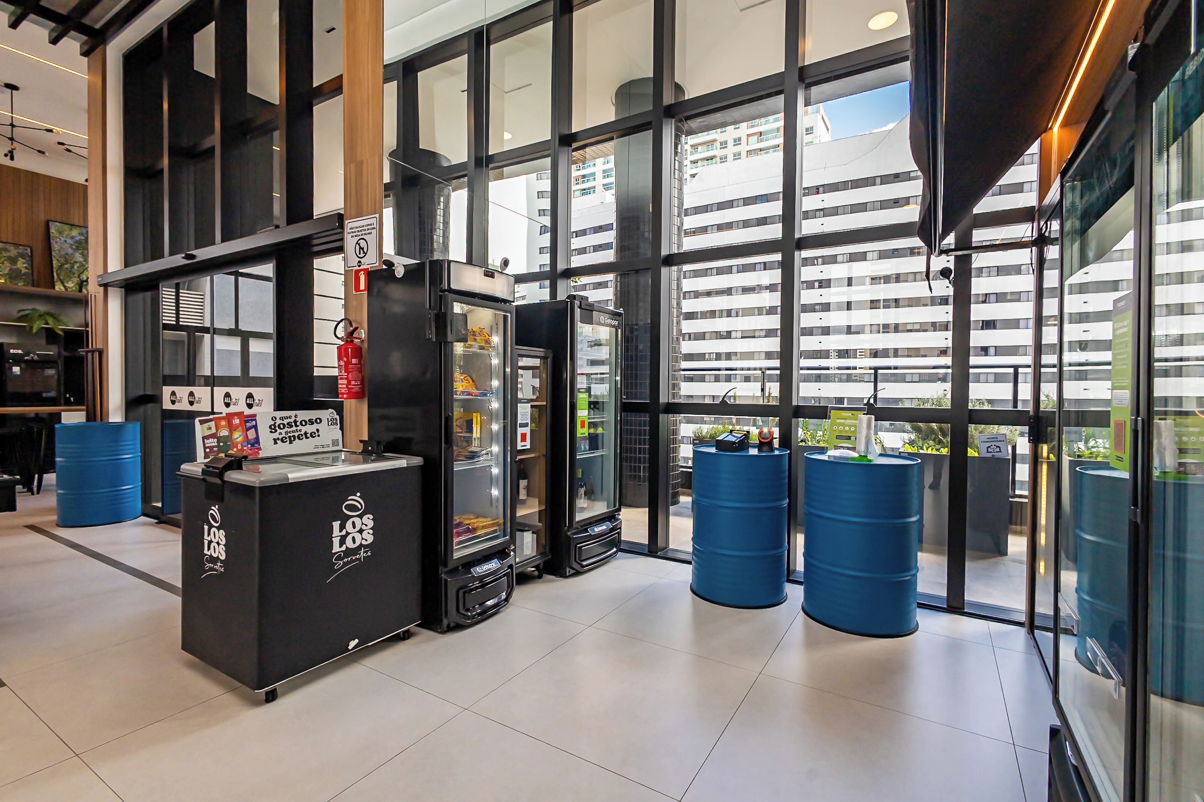 A modern interior with large windows, a reception desk, and blue barrels.
