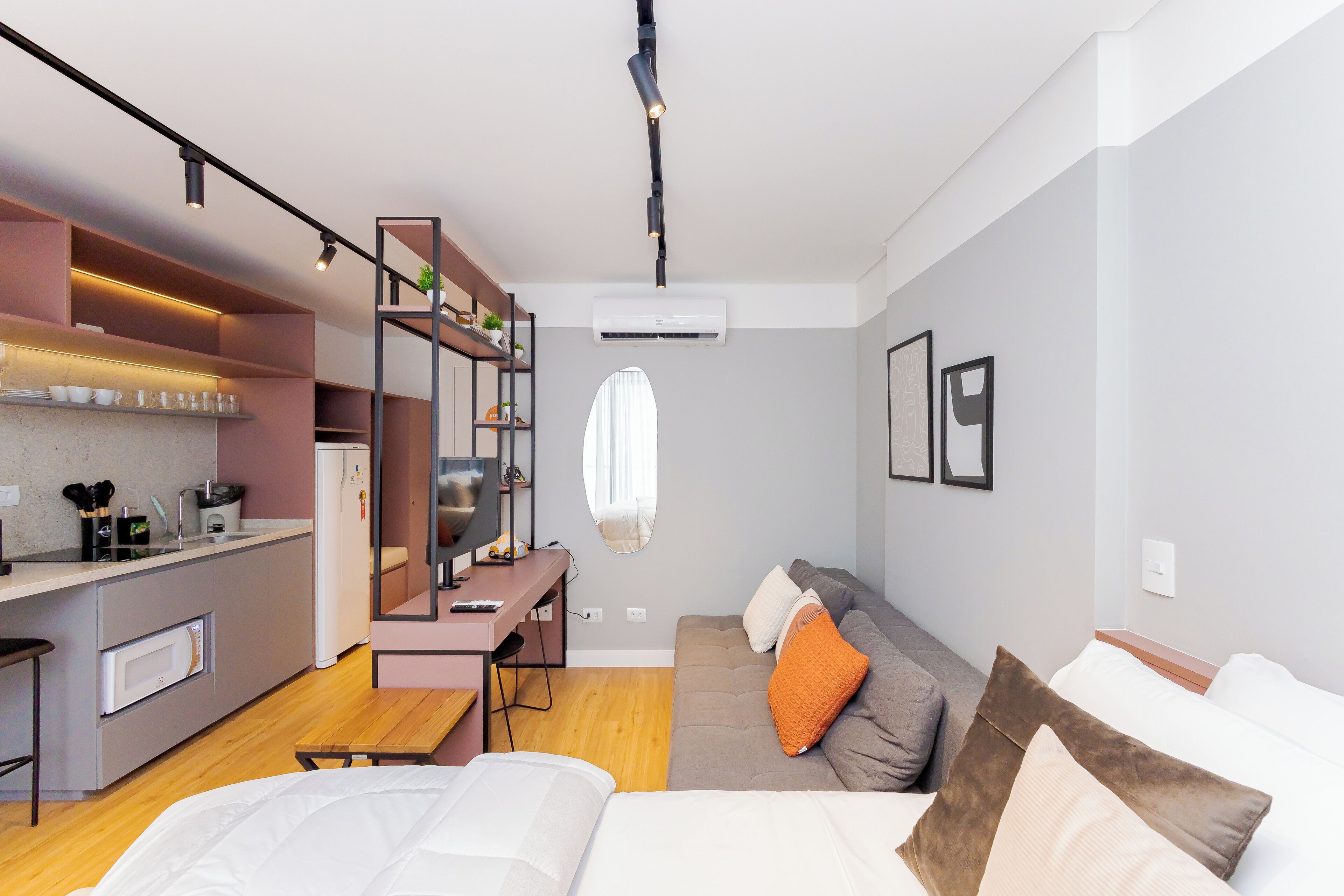 A modern hotel room with a kitchenette, a sofa bed, and a desk with a chair.