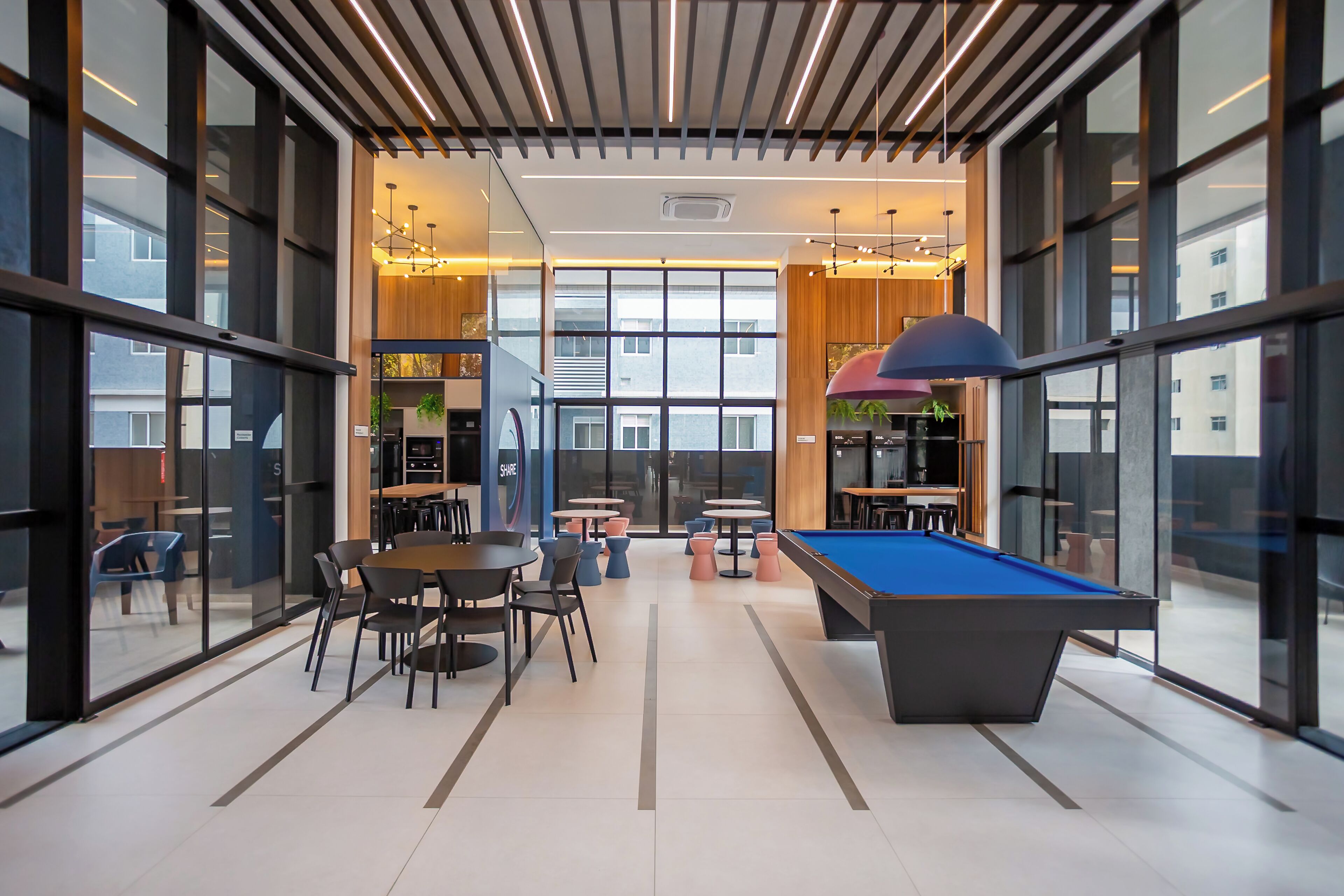 A modern indoor recreational area with a pool table, seating, and large windows offering views of the city.