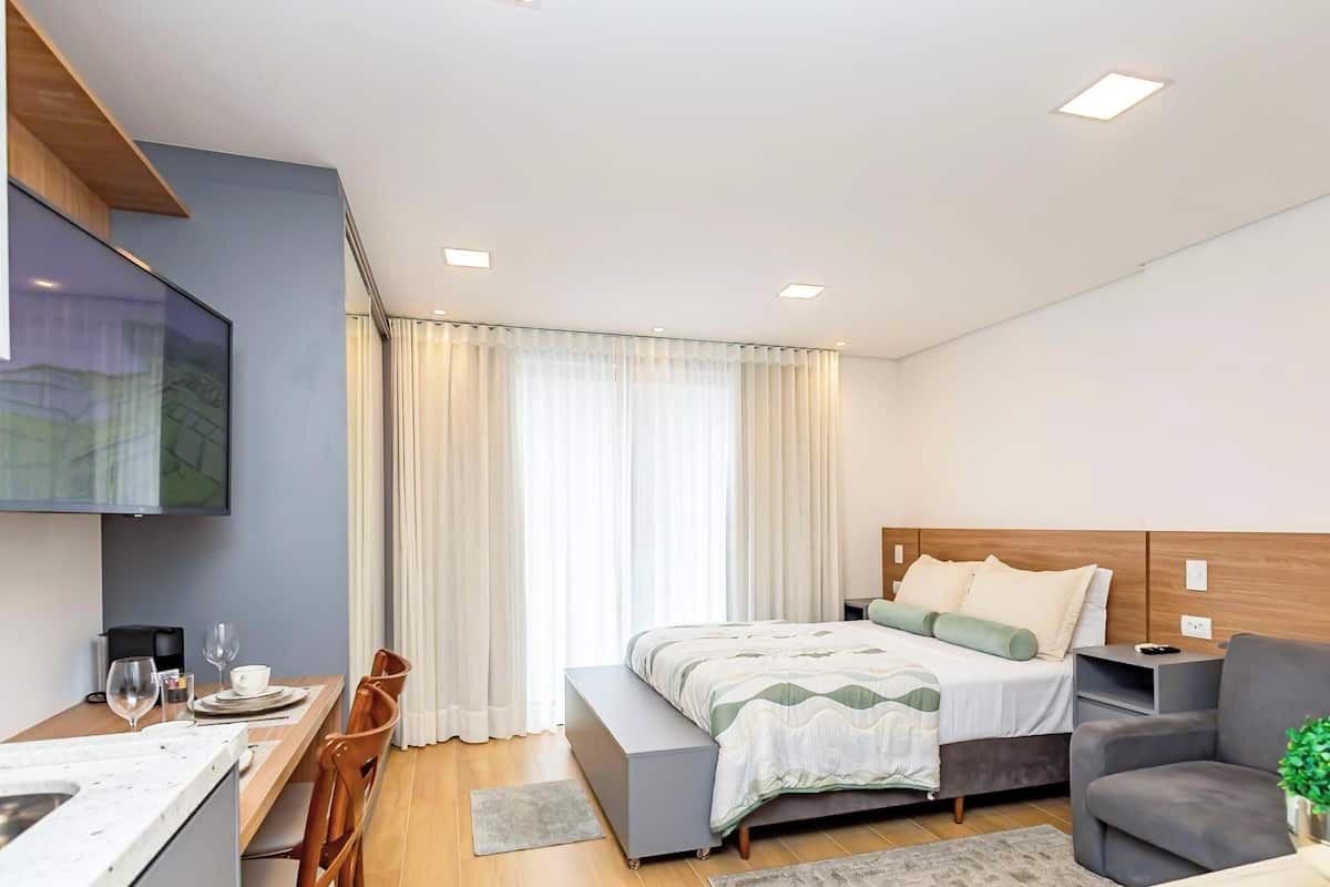 A modern hotel room with a bed, bedside table, and a small seating area.