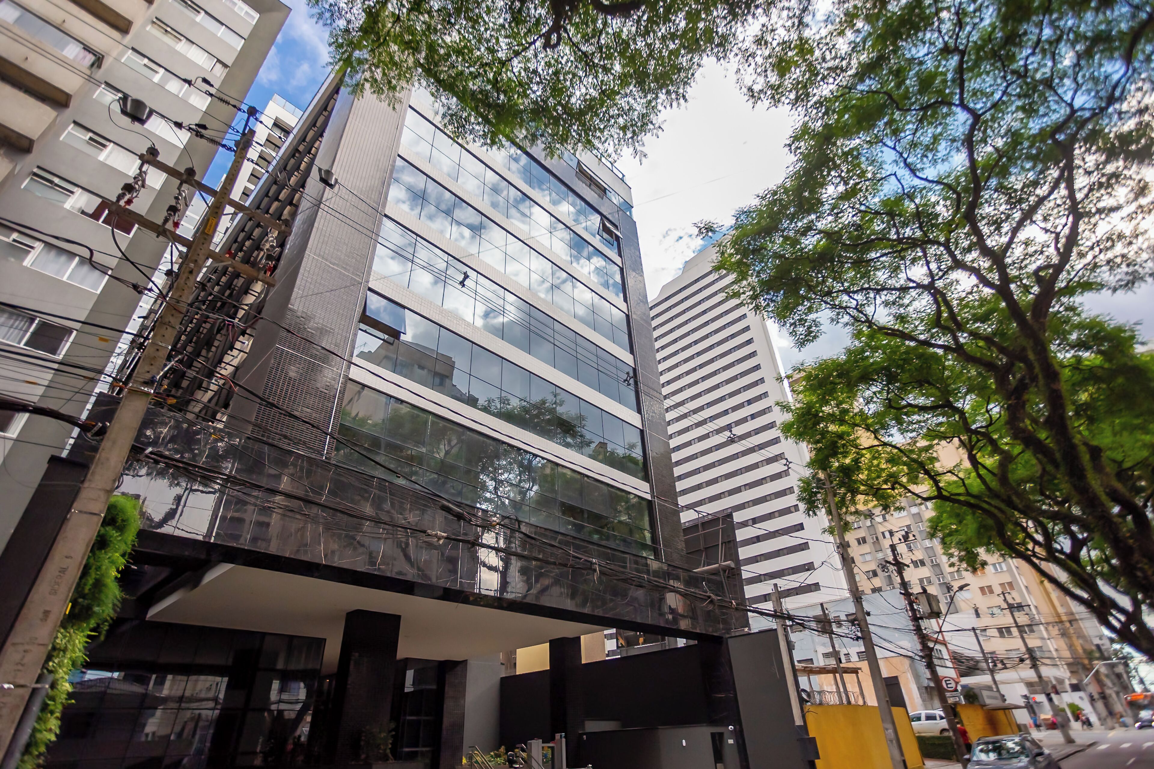 A modern building with a glass facade, multiple floors, and a pedestrian bridge.