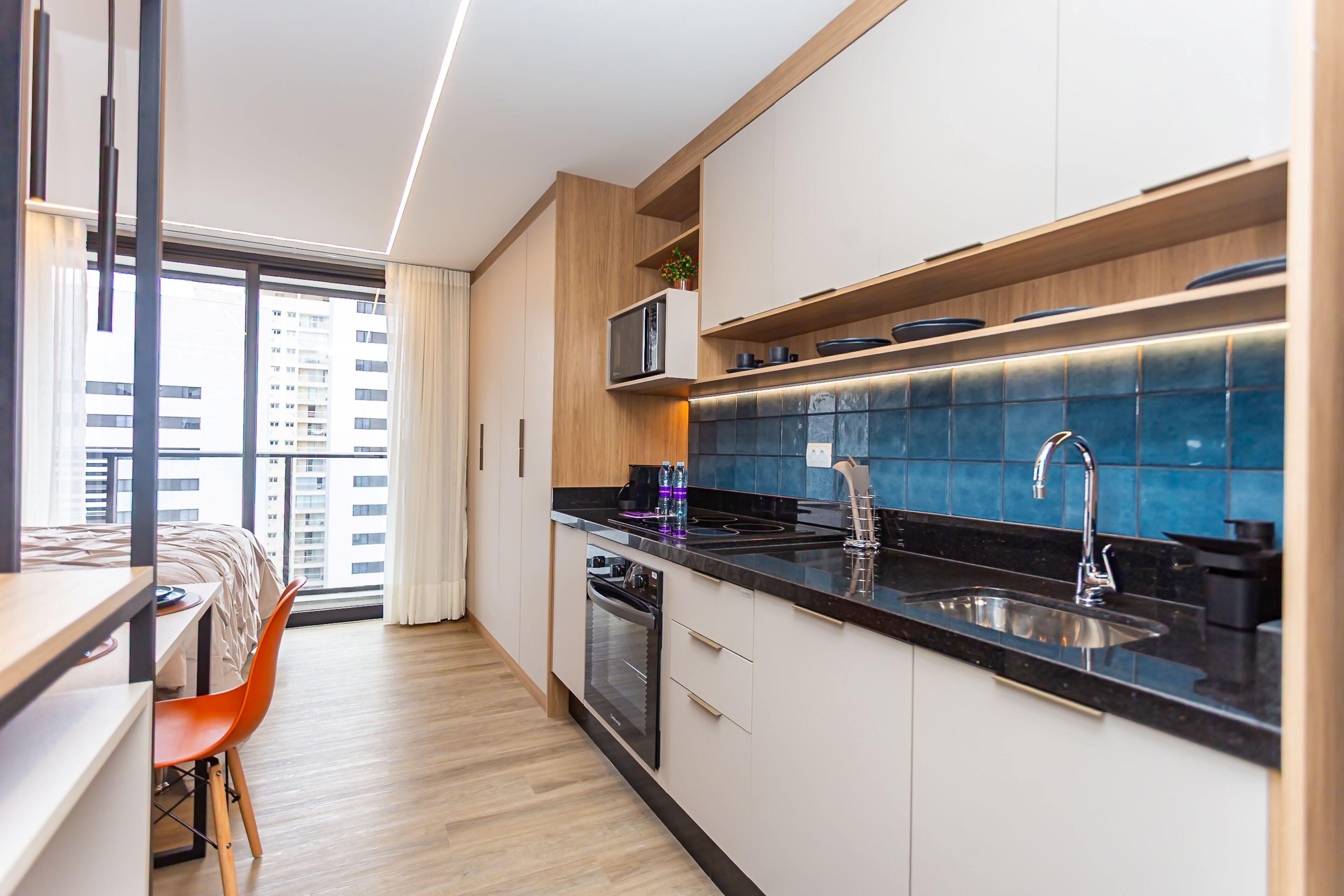 Cocina moderna con horno empotrado, microondas y lavamanos. Hay un comedor con mesa y sillas, y un ventanal con vistas a la ciudad.