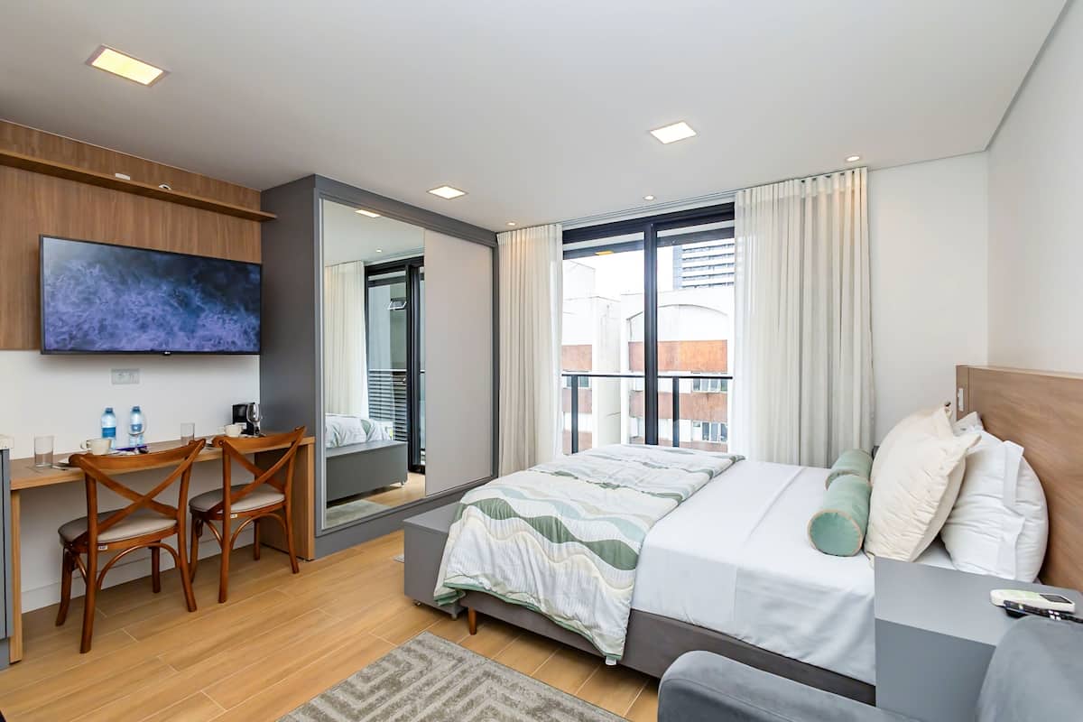 A hotel room with a bed, a desk with chairs, a TV, and a large window.