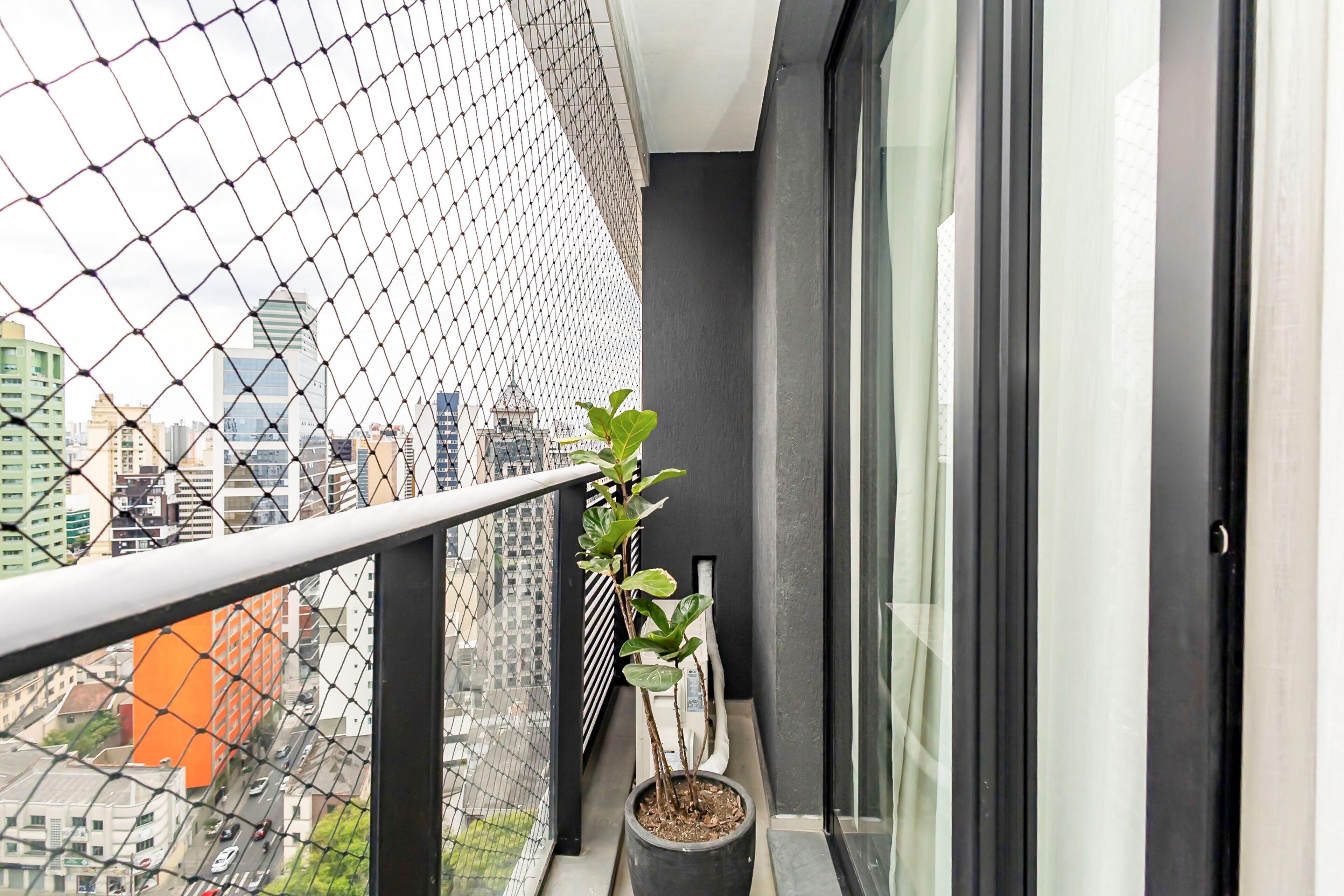 A balcony with a chain-link fence, a potted plant, and a cityscape view.