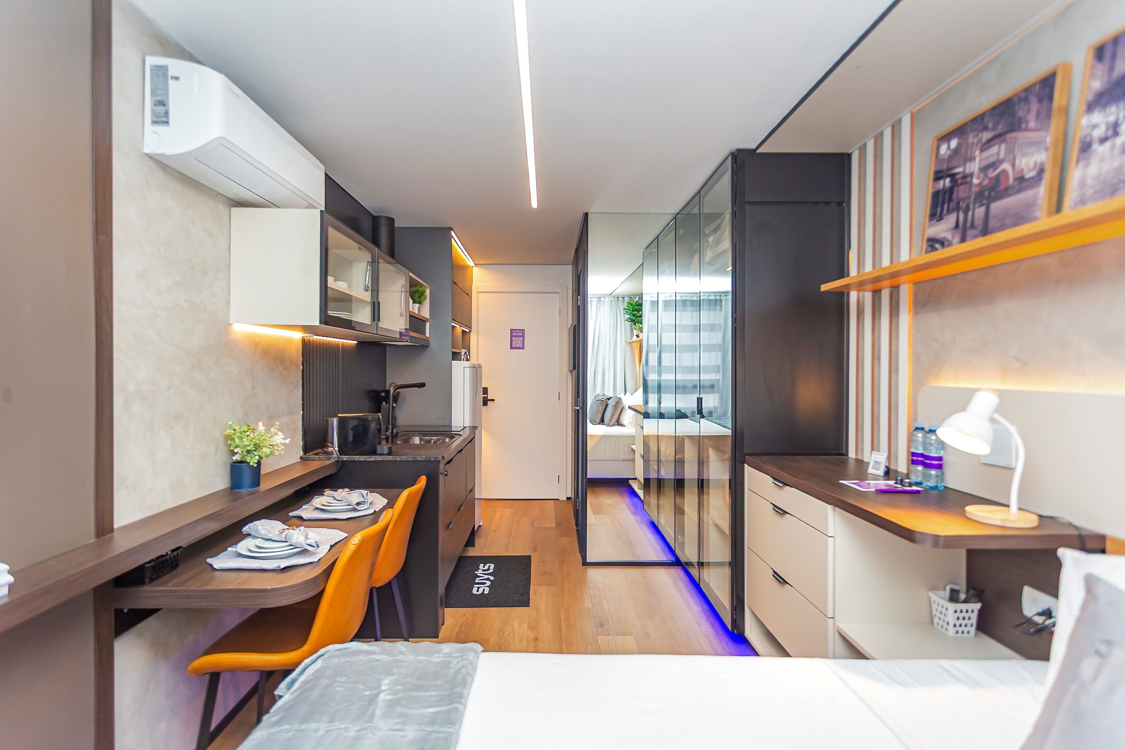 A modern, compact hotel room with a kitchenette, a bed, a desk, and a small seating area.