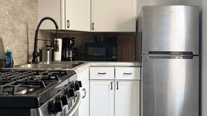 A modern kitchen with white cabinets, a stainless steel refrigerator, a gas stove, and a microwave. - Downtown EVV Studio / Chandler C (Evansville)