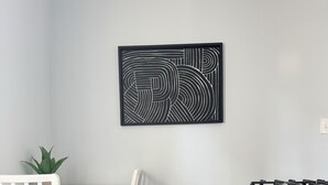 A kitchen with a white dining table, white chairs, a modern stove, and a black abstract artwork on the wall. - Downtown EVV Studio / Chandler C (Evansville)