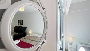 A hotel room with a large mirror, a bed with a red blanket, a bedside table with a lamp, and a window with blinds. - Modern & Cozy Studio San Telmo With Pool and Exclusive Services (Buenos Aires)
