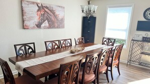 A dining room with a wooden table, six chairs, a chandelier, a painting, and a cabinet.