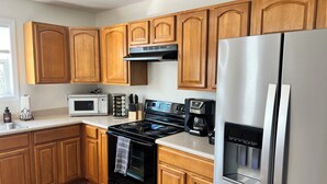 A modern kitchen with wooden cabinets, a stainless steel refrigerator, a microwave, a stove, and a coffee maker.