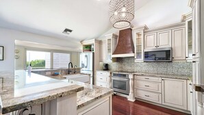 A spacious kitchen with white cabinetry, a granite countertop, a stainless steel range, and a large island with a sink.