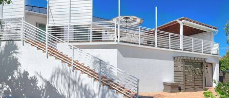 A modern building with a staircase leading to a balcony, a covered outdoor area, and a large wooden door.