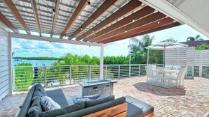 A covered outdoor patio with a stone fireplace, a wooden bench, and a table with chairs.