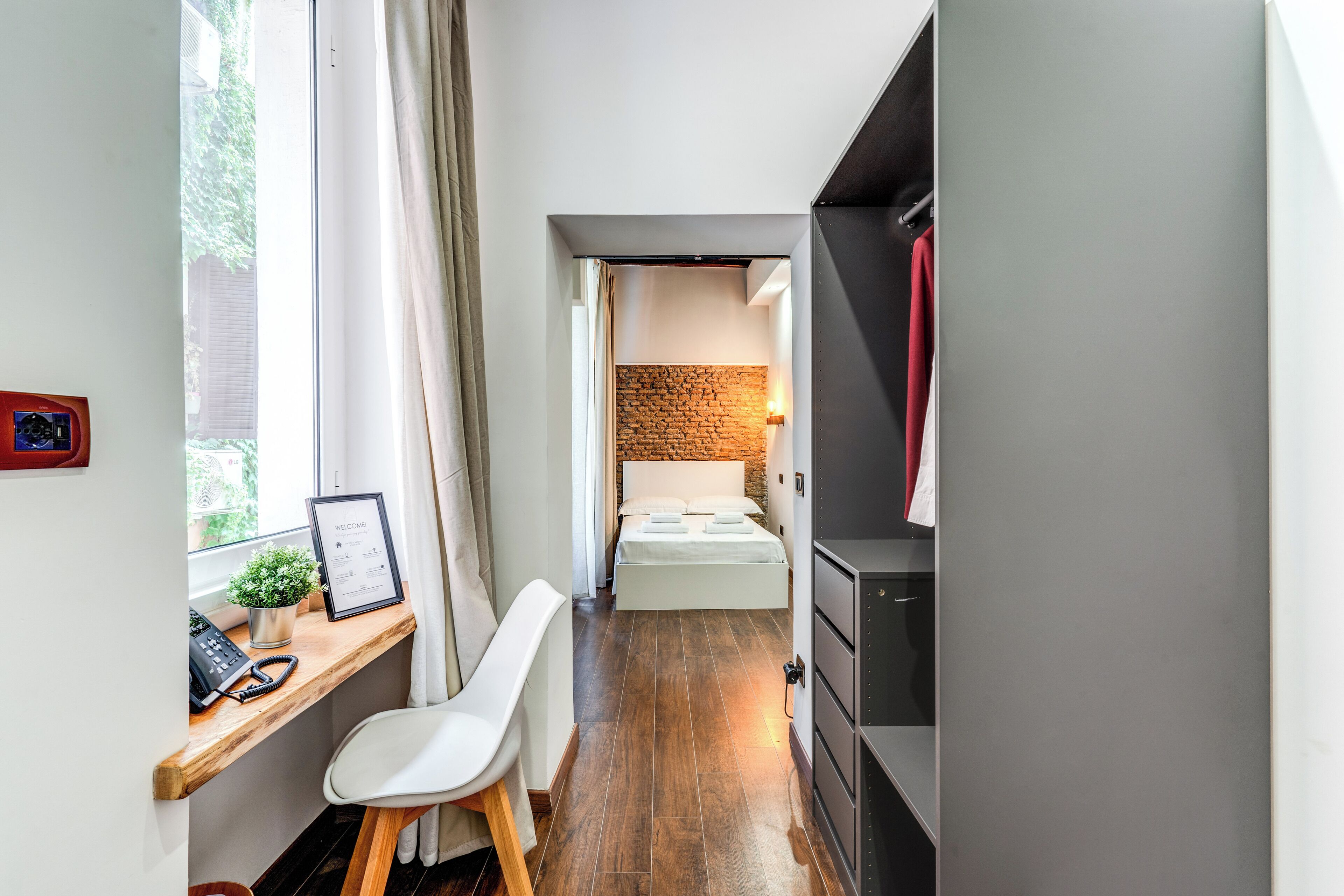 A compact hotel room with a desk, chair, bed, and a small seating area.