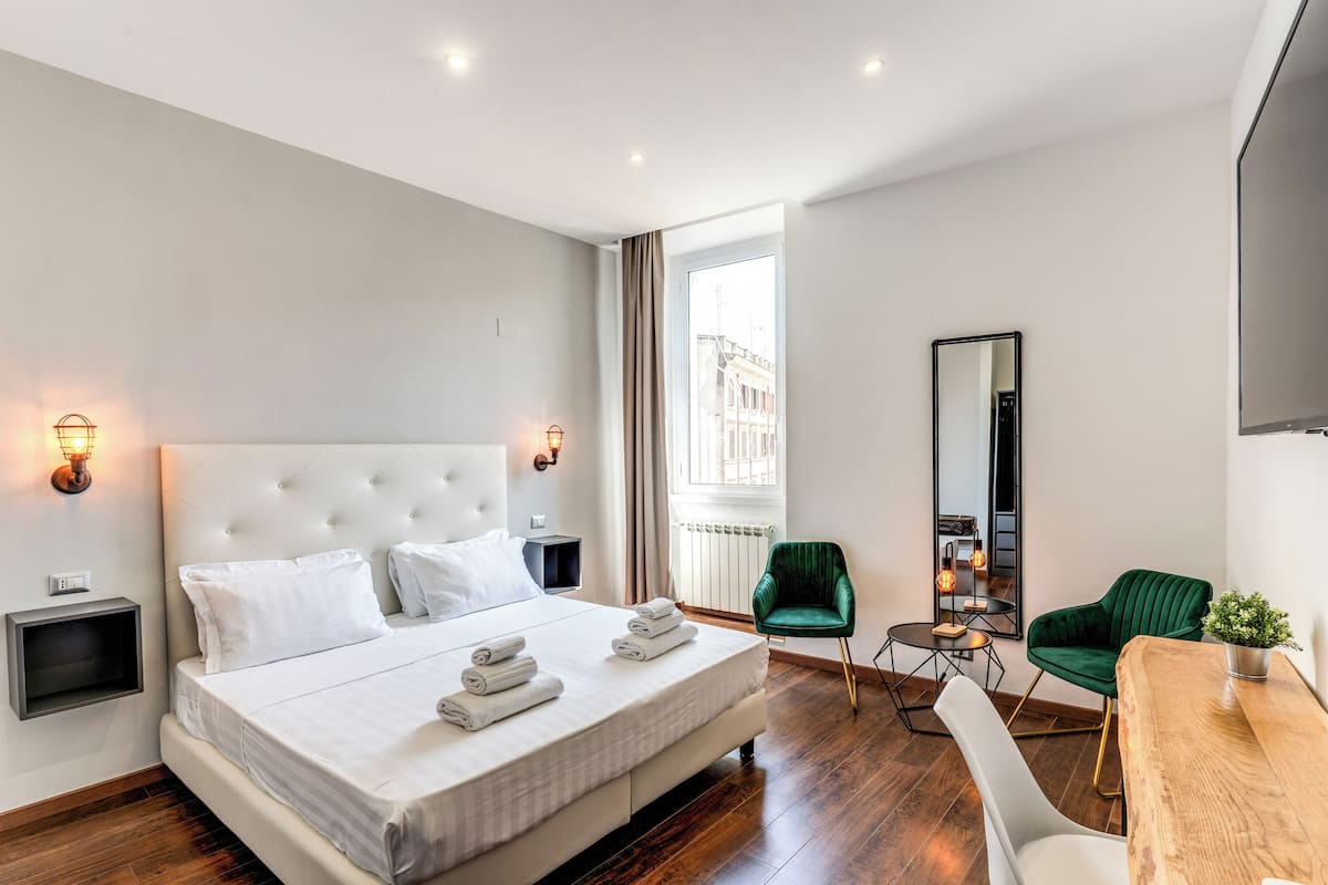 Ein modernes Hotelzimmer mit einem großen Bett, einem Schreibtisch, einem grünen Sessel und Blick auf die Stadt.