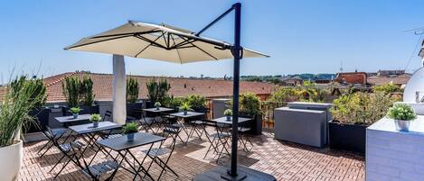 Une terrasse sur le toit avec des sièges extérieurs, un grand parasol et des plantes en pot.