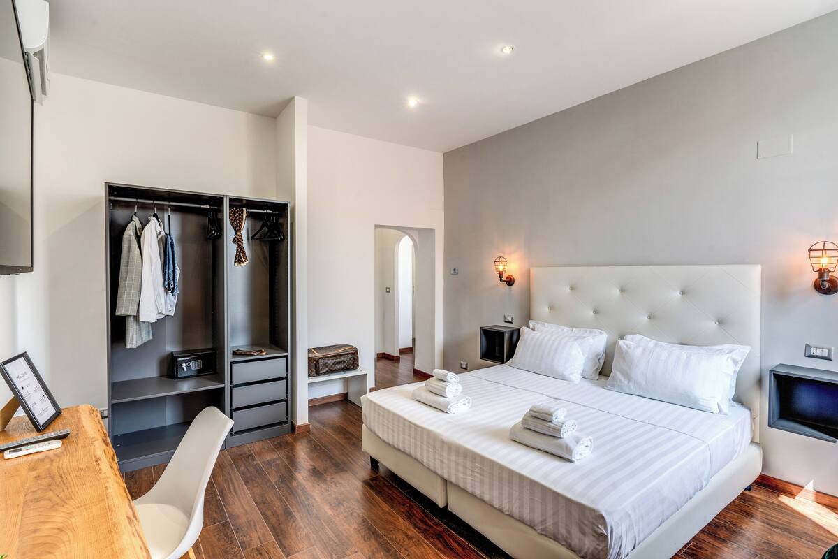 Ein modernes Schlafzimmer mit einem großen Bett, einem Kleiderschrank, einem Schreibtisch und einem Fernseher.