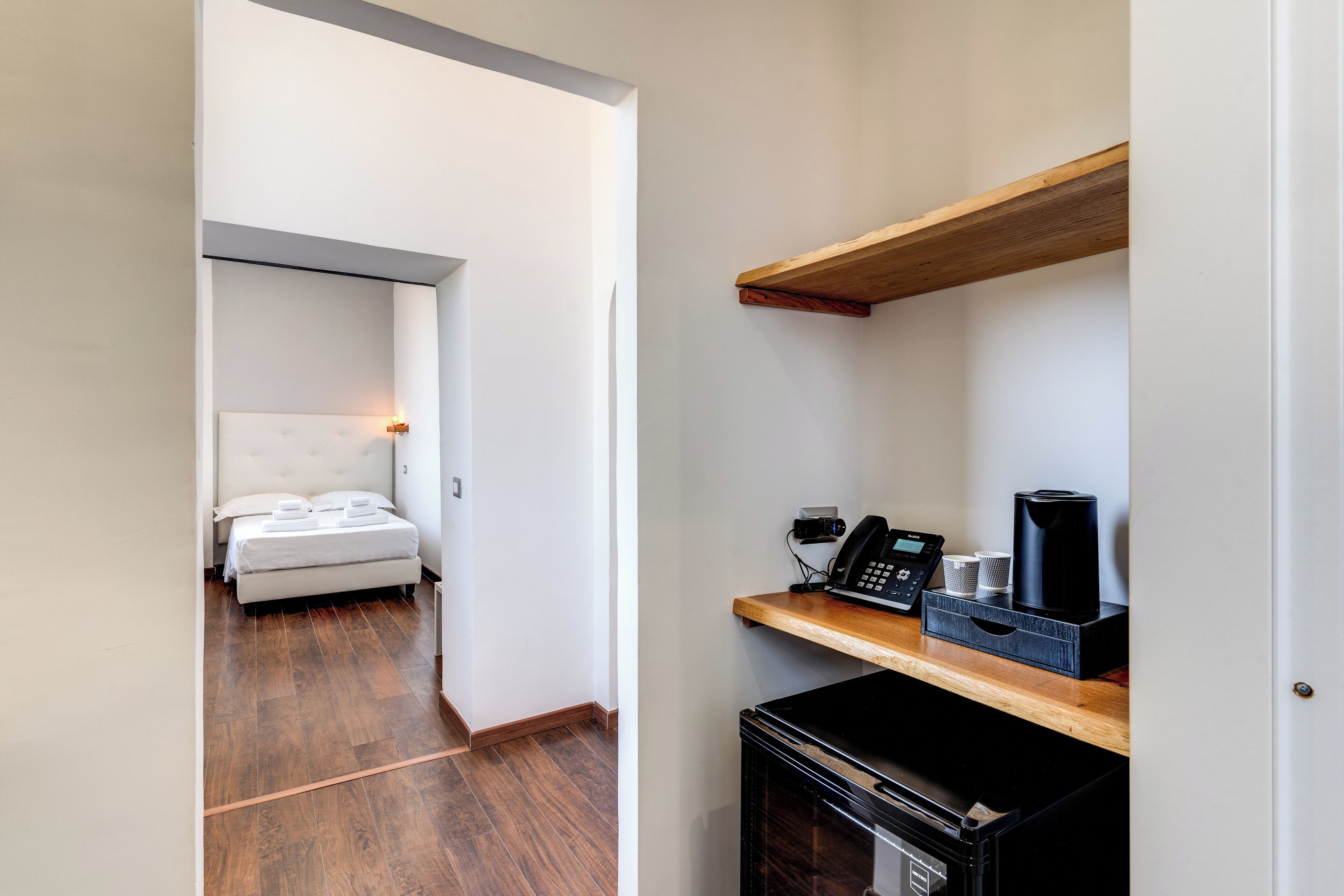 A hotel room with a bed, a coffee machine, and a microwave on a wooden shelf.