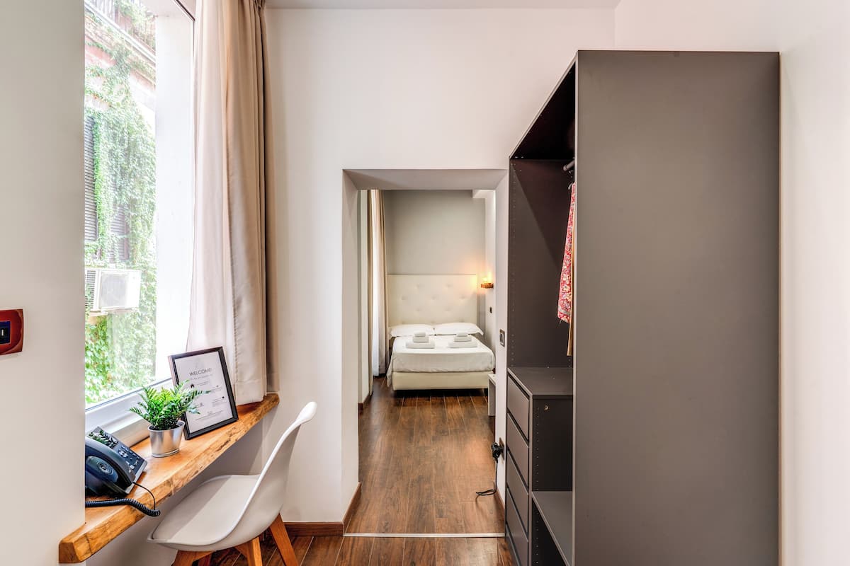 Ein schmaler Flur führt zu einem Schlafzimmer mit Bett, Nachttisch und Schreibtisch, inklusive Telefon und einer Willkommensanzeige.