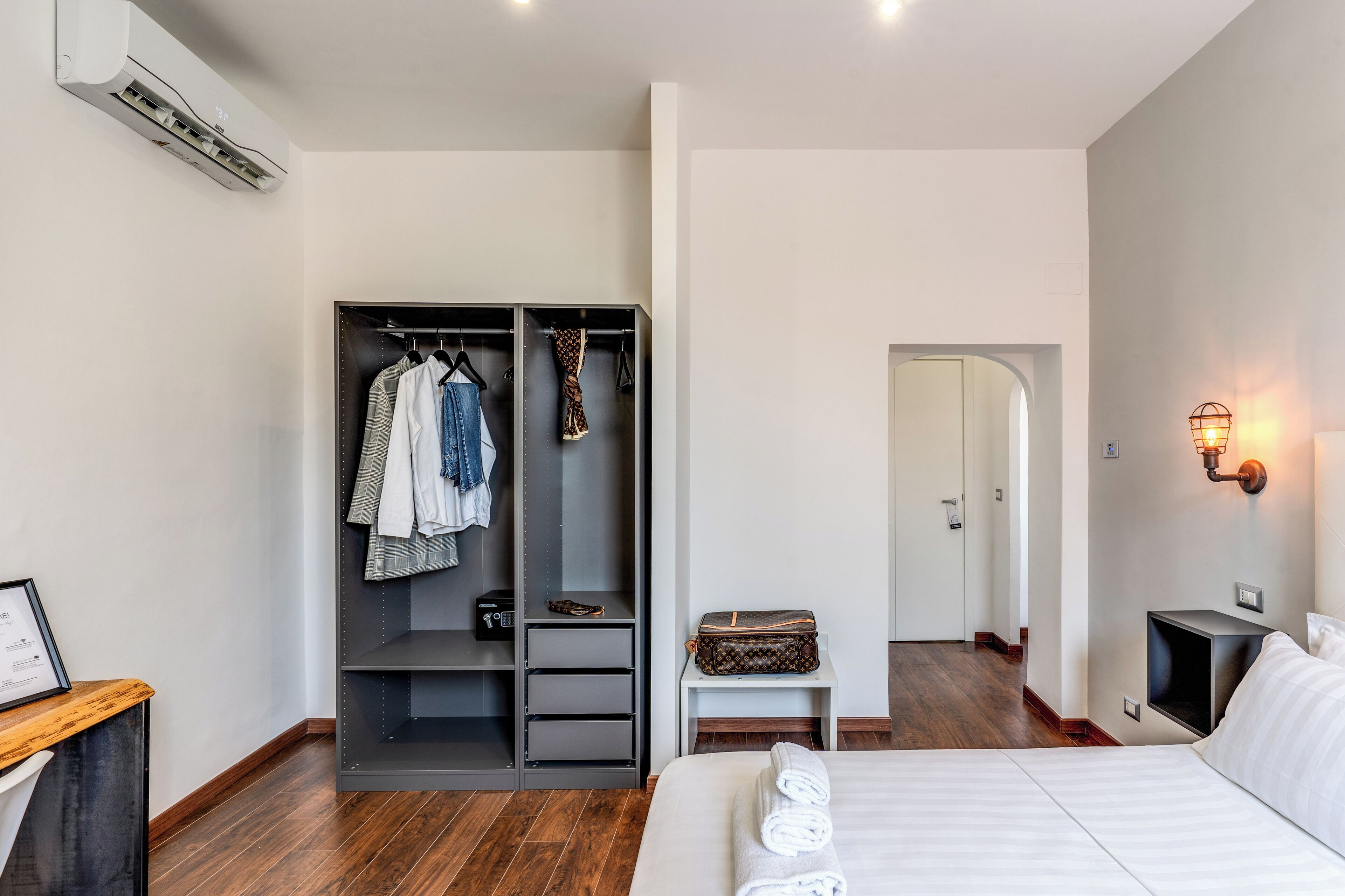 Habitació d'hotel moderna amb un llit, un armari, una taula de nit i una estanteria.