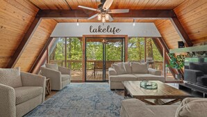 A cozy, wooden-floored living room with a ceiling fan, a large window, and a sign reading "lakelife".