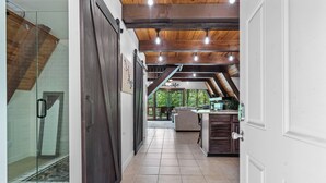 A spacious hallway with a wooden ceiling, a glass door leading to a shower area, and a kitchen area with a counter and cabinets.