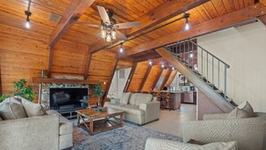 A spacious living area with a high ceiling, wooden beams, a fireplace, and a staircase leading to an upper level.