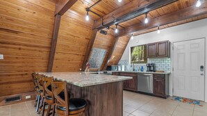 A kitchen with a wooden ceiling, a central island with bar stools, and a view of the outdoors through a window.