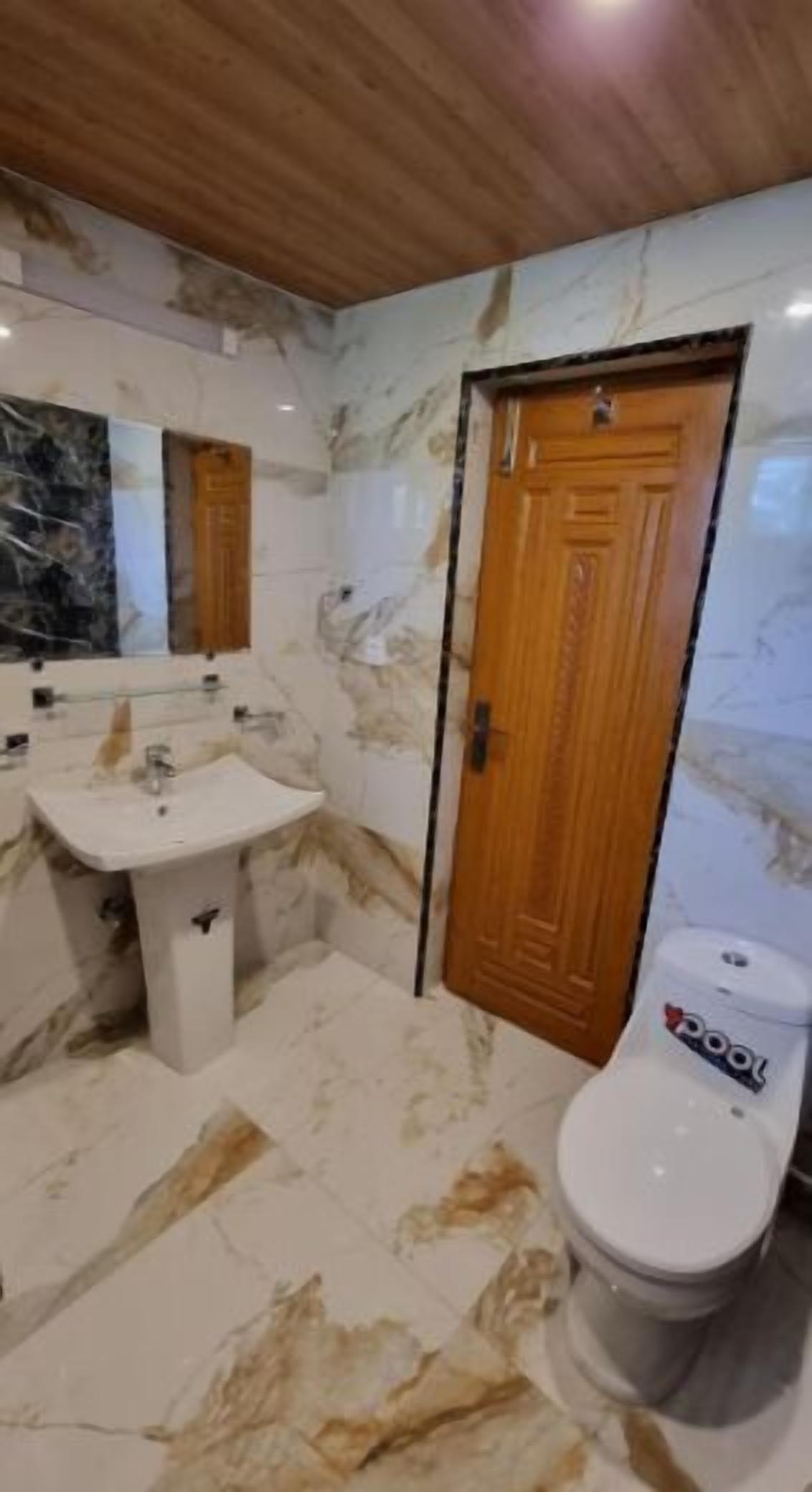 A bathroom with a marble floor, a sink, a toilet, and a wooden door.