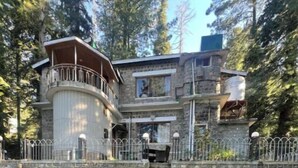 A two-story stone house with a balcony, a stone wall, and a grassy lawn.