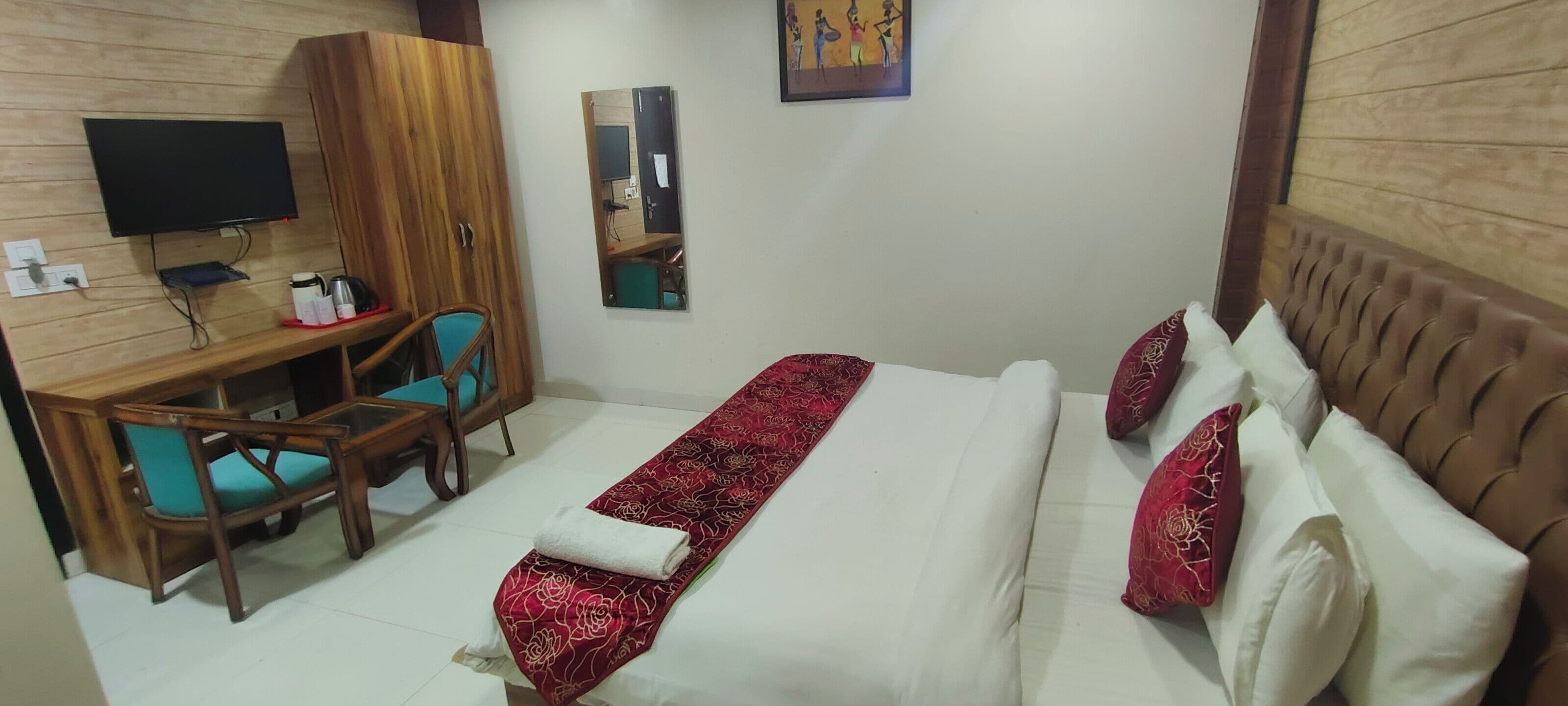A hotel room with a bed, a desk with a chair, a television, and a mirror.