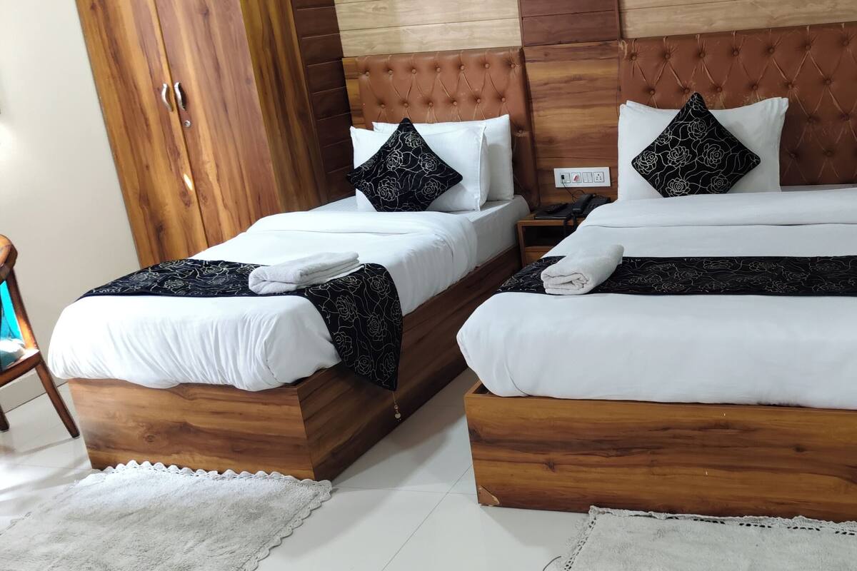 Une chambre d’hôtel avec deux lits en bois, chacun agrémenté de draps blancs et d’oreillers noirs à motifs floraux.