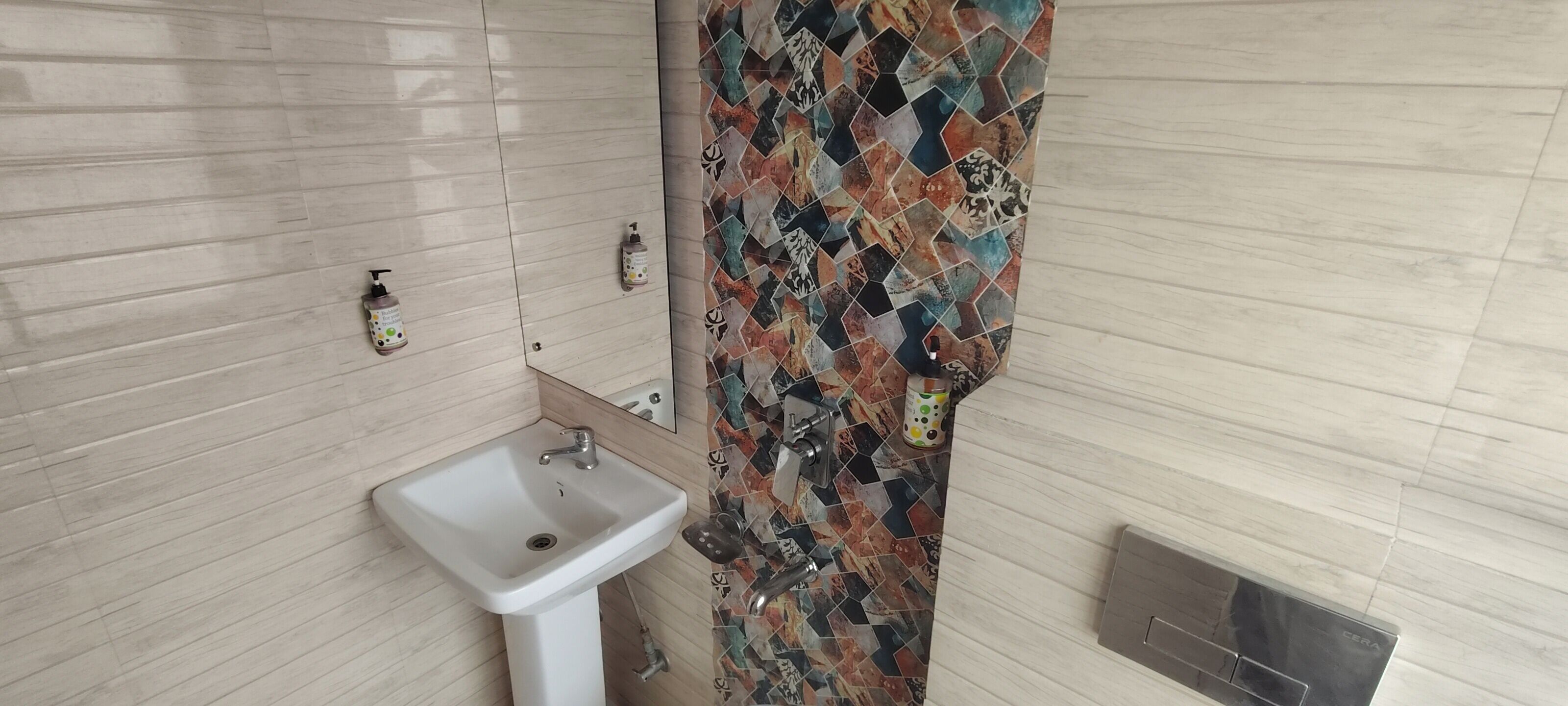 Ein Badezimmer mit weißem Waschbecken, einer gefliesten Duschkabine und einem Handtrockner an der Wand.