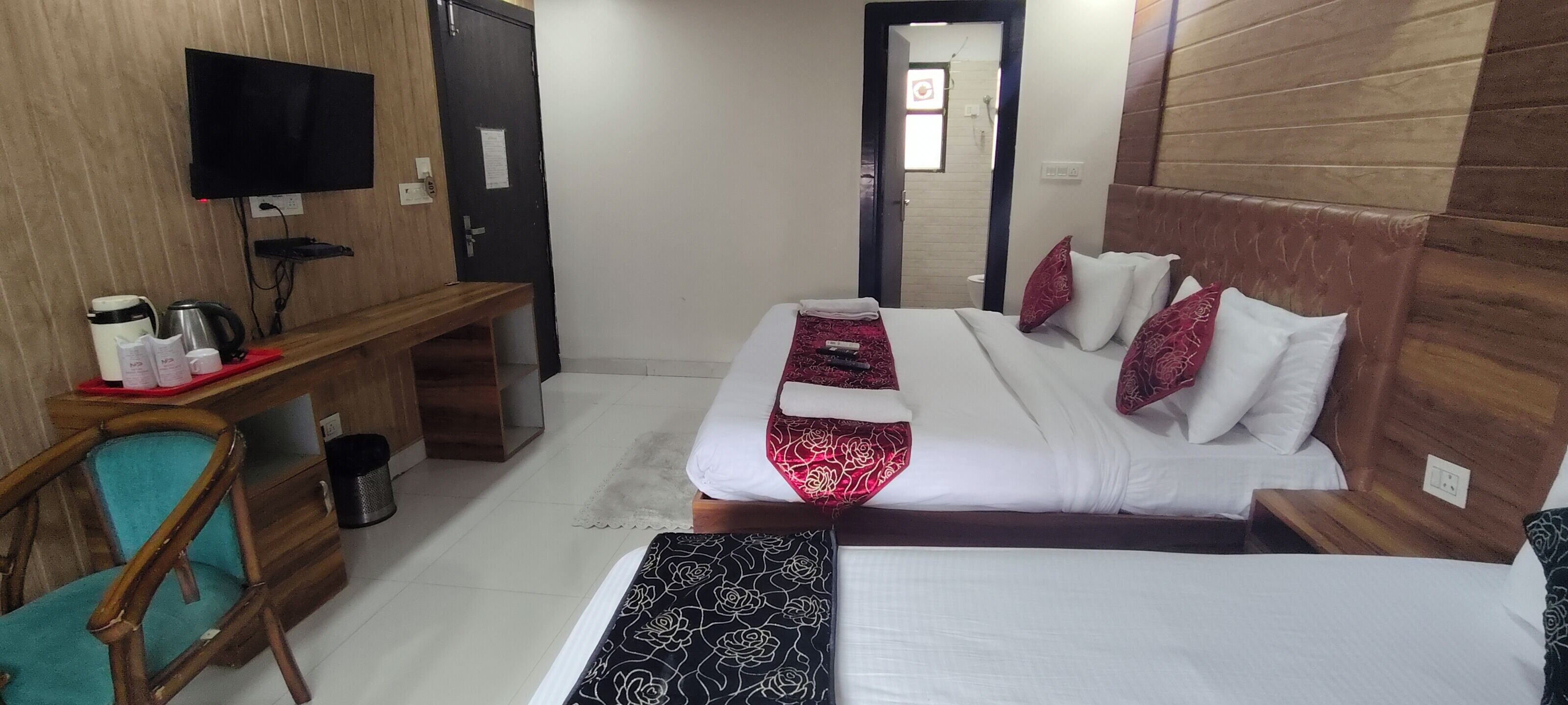 Camera d'albergo con un letto, una scrivania con televisore, una sedia e un tavolino con bollitore e tazze.