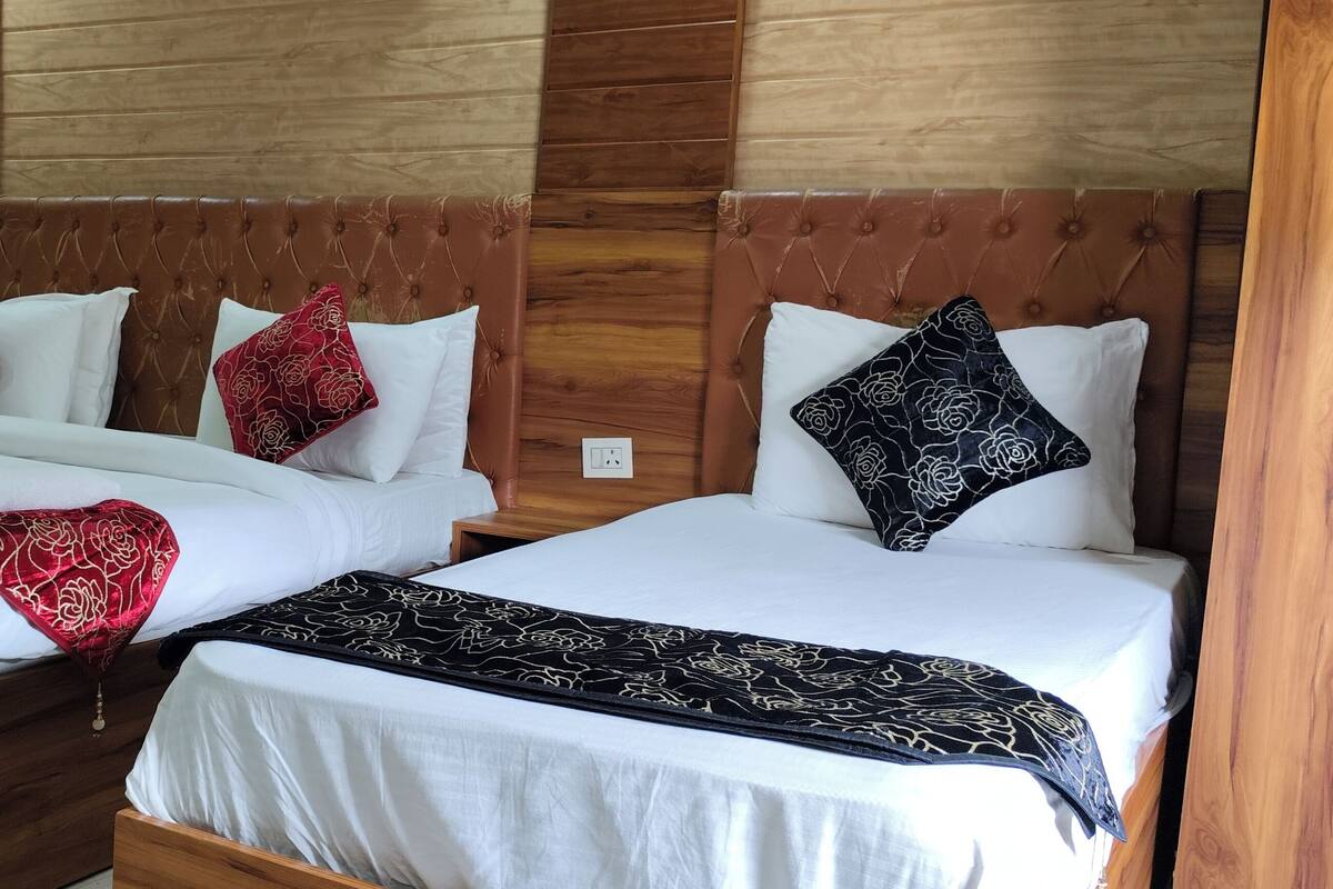 Deux lits doubles avec des têtes de lit en bois, du linge de lit blanc et des coussins décoratifs.