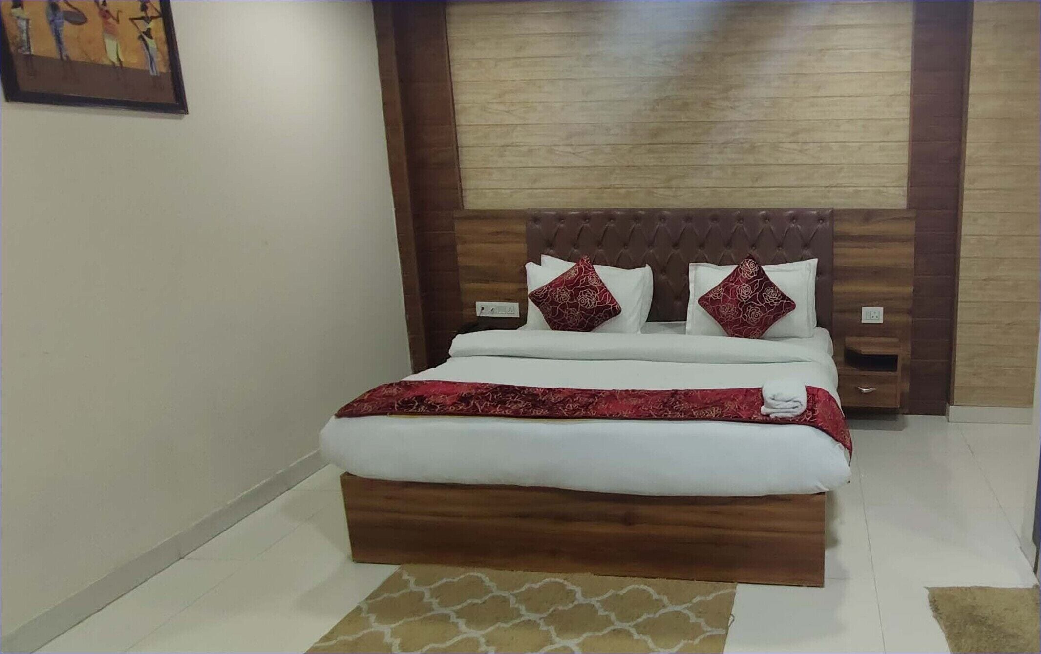 Una cama bien hecha con cabecera de madera, dos almohadas y una colcha estampada roja.