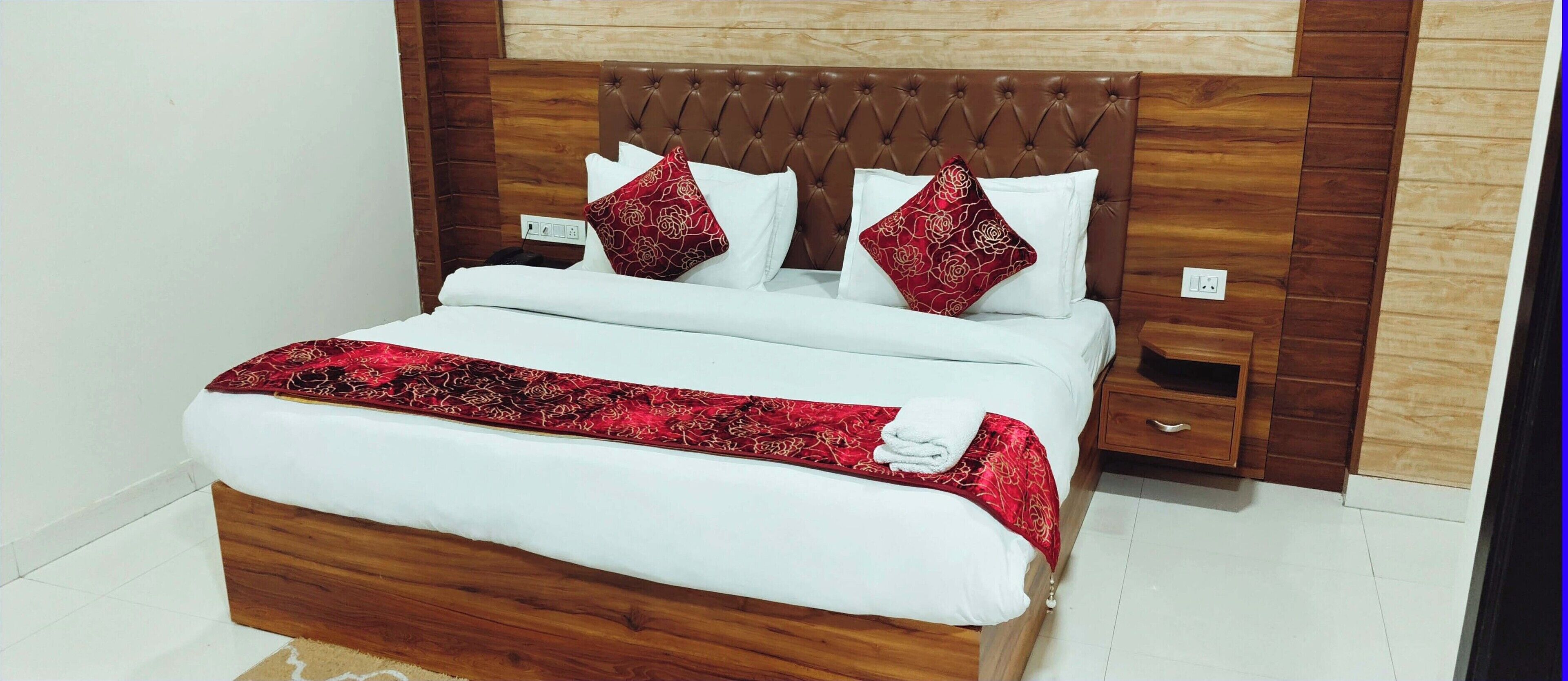 A neatly made bed with a red and white patterned bedspread, a wooden headboard, and two decorative pillows.