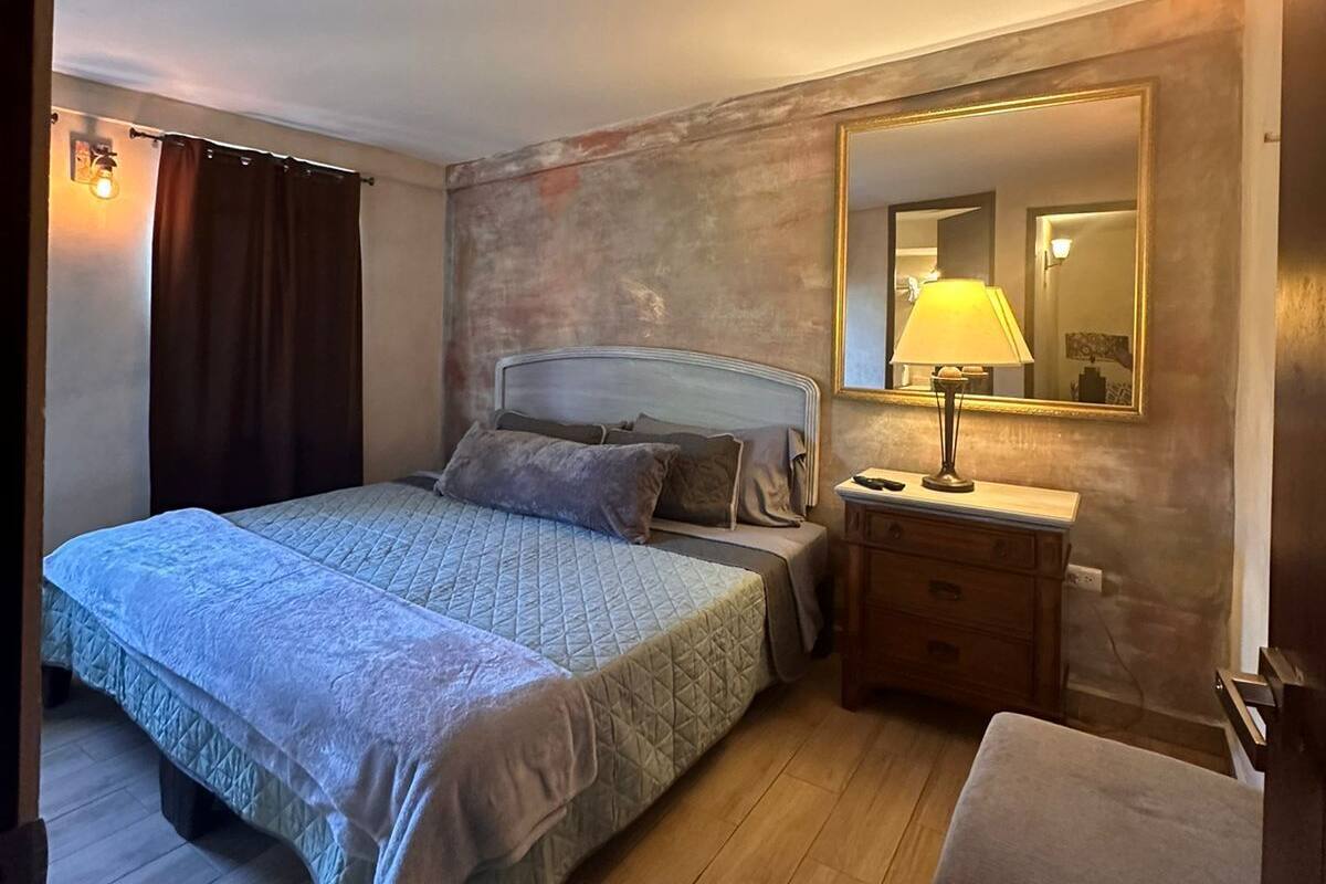 Un dormitorio con cama, mesita de noche, silla y un espejo grande.