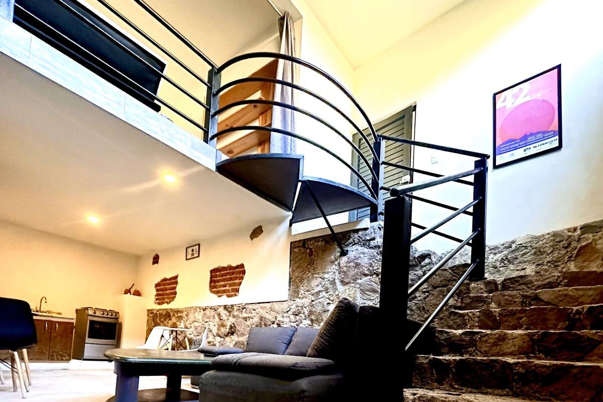 Amplia sala de estar con una escalera de piedra, una mesa de comedor y un sofá.