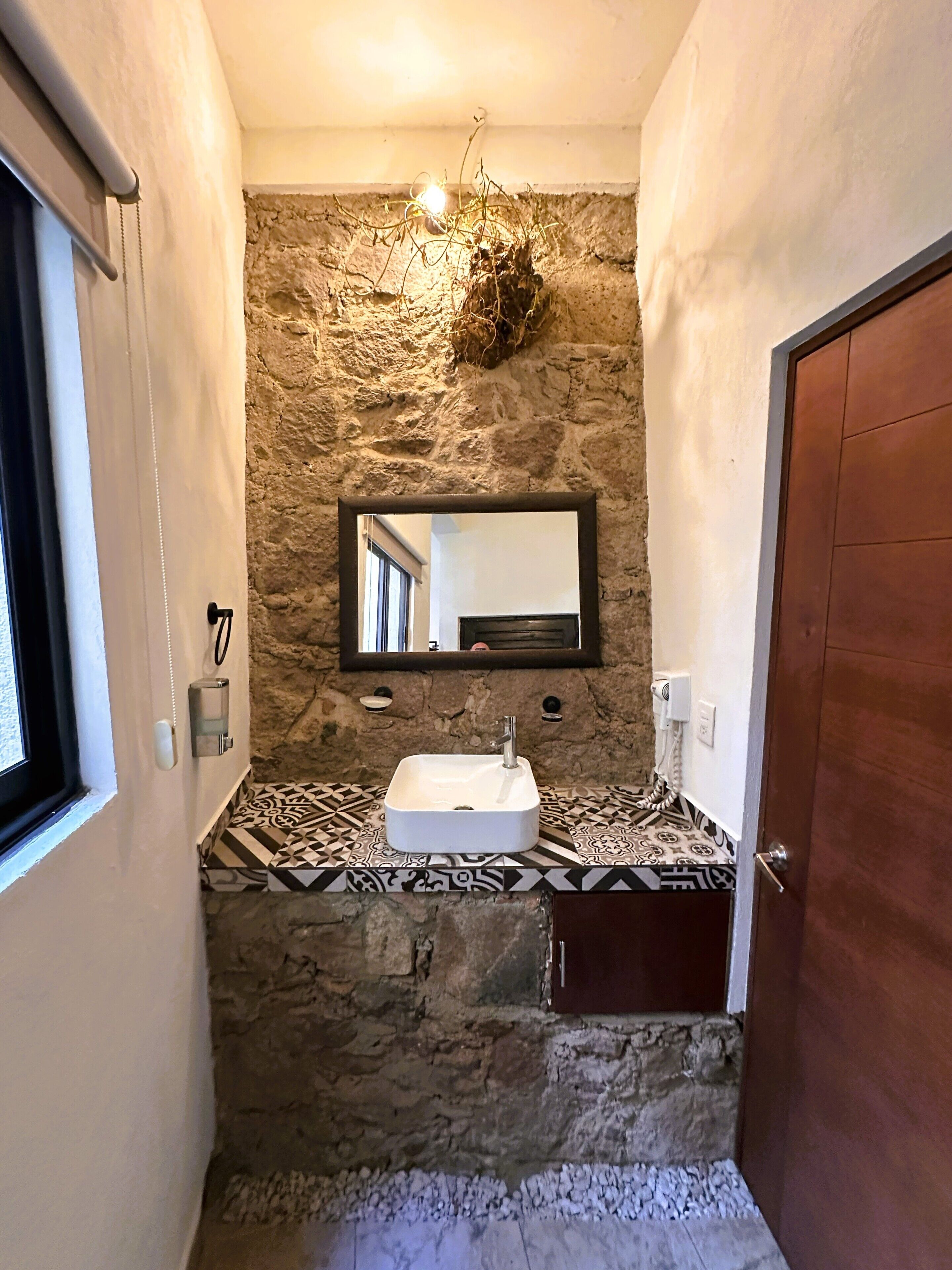 A bathroom with a stone wall, a sink, a mirror, and a door.