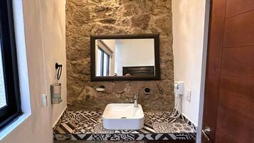 A bathroom with a stone wall, a sink, a mirror, and a door.